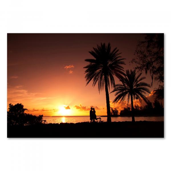 Silhouetten eines Paares, das sich vor dem malerischen Sonnenuntergang am Strand küsst, umgeben von Palmen.